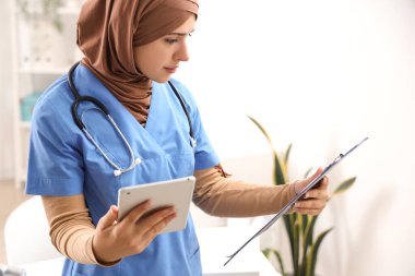 Klinikte panosu ve tablet bilgisayarı olan kadın Müslüman doktor