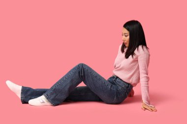 Pembe arka planda oturan şık kotlu güzel Asyalı kadın.