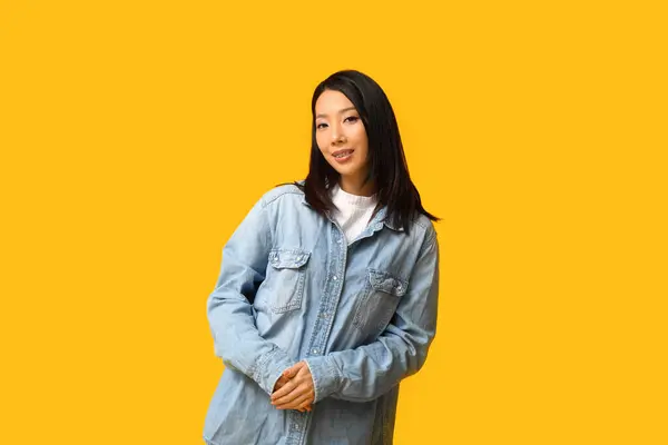 黄色の背景にスタイリッシュなデニムジャケットで美しい若い幸せなアジアの女性 — ストック写真