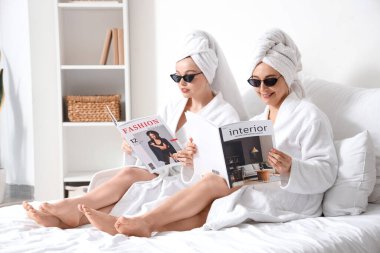 Genç bir kadın ve annesi yatak odasında duştan sonra dergi okuyorlar.