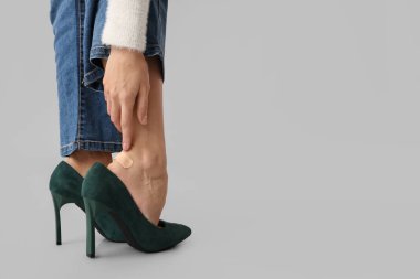 Yüksek topuklu ayakkabılı genç bir kadın gri arka planda ayak üstüne sıva uyguluyor. Rahatsız ayakkabı konsepti