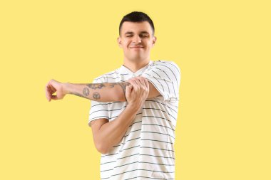 Sarı arka planda kol ağrısı çeken genç bir adam.