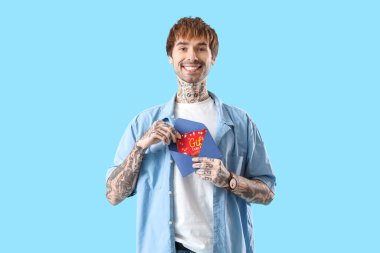 Mavi arka planda zarfta hediye kartı olan dövmeli genç bir adam.