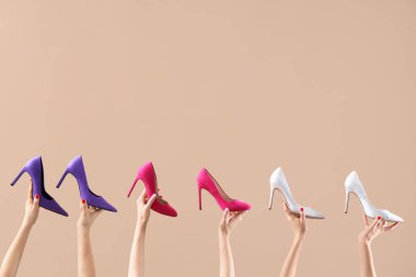 Bej arka planda farklı ayakkabılar tutan kadın eller.