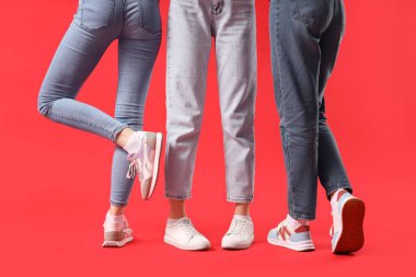 Kırmızı arka planda farklı ayakkabılar giyen kadın bacakları.