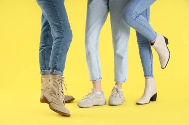 Sarı arka planda farklı ayakkabılar giyen kadın bacakları.