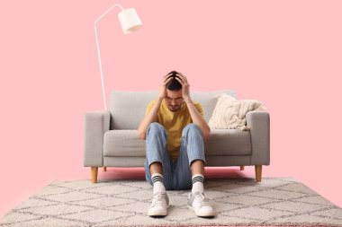 Genç adam pembe arka planda kanepenin yanında baş ağrısı çekiyor.