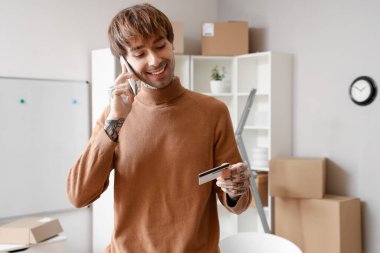 Depoda cep telefonuyla konuşan kredi kartı olan genç bir satıcı.