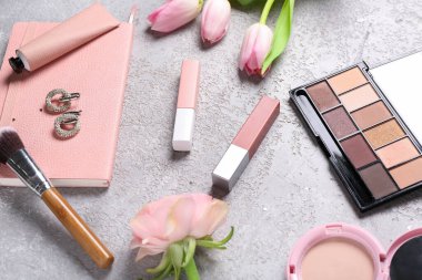 Çiçekli defter, makyaj ürünleri ve gri grunge arka planda küpeler.