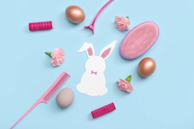 Paskalya yumurtalı kağıt tavşan, çiçekler ve mavi arka planda kuaför aksesuarları.