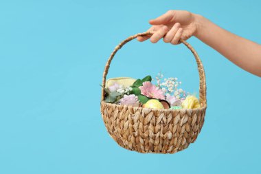 Makyaj ürünleri, çiçekler ve mavi arka planda Paskalya dekoru olan kadın el ele tutuşma sepeti