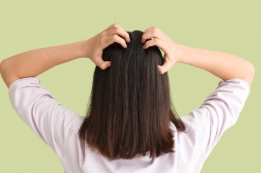 Kepek sorunu olan genç bir kadın yeşil arka planda kafasını kaşıyor.