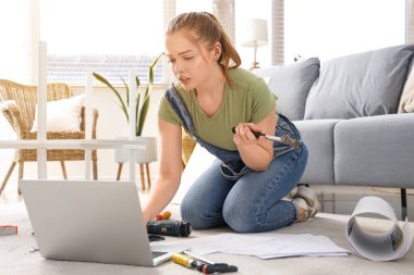 Evde mobilya montajı yapan dizüstü bilgisayarı ve çekici olan güzel genç bir kadın.