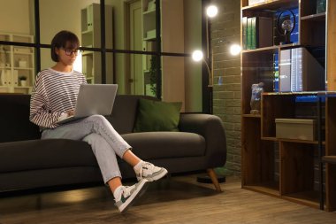 Geceleri koltukta dizüstü bilgisayarla çalışan kadın programcı.