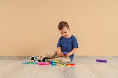 Otistik bozukluğu ve bej duvarın yanında oyuncakları olan küçük bir çocuk.