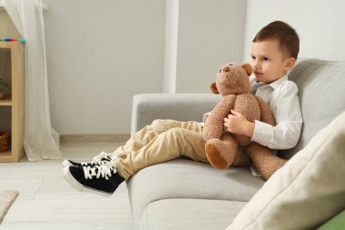 Otistik bozukluğu olan küçük bir çocuk ve evdeki kanepede oturan oyuncak ayı.