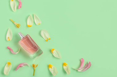 Yeşil arka planda taç yaprakları olan pembe parfüm şişesi. Üst görünüm