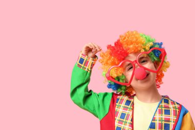 Pembe arka planda kalp şeklinde gözlükleri olan palyaço kostümlü komik çocuk. 1 Nisan şakası