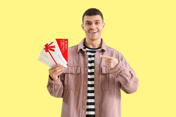 黄色い背景のギフト券を指している若い男 — ストック写真