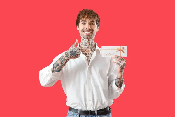 Jovem Tatuado Homem Apontando Para Cartão Presente Fundo Vermelho — Fotografia de Stock