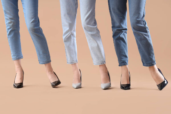На бежевом фоне женские ноги в разных туфлях на высоких каблуках