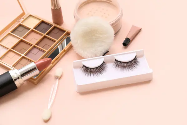 Makeup products with fake lashes on beige background