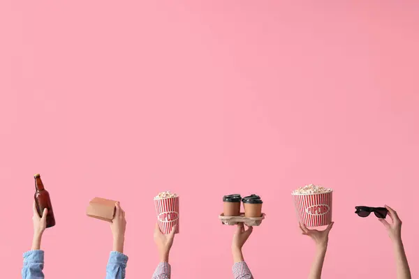 Many hands with buckets of popcorn, beer and coffee on pink background
