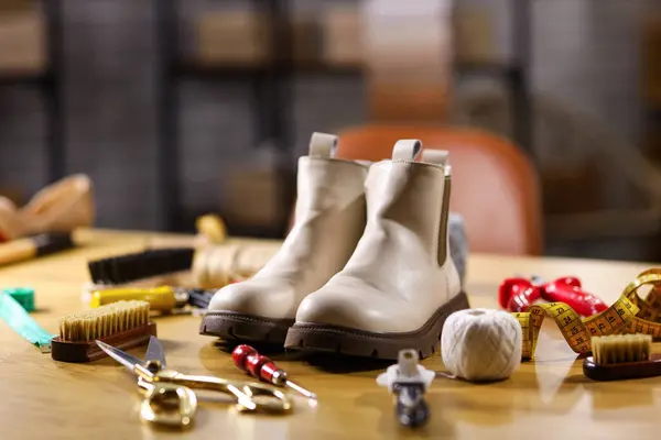 Boots with shoemaker\'s tools on table in workshop, closeup