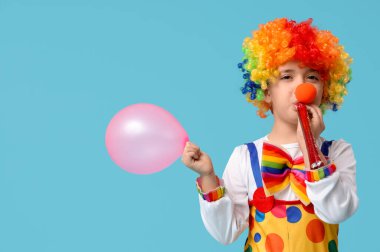Mavi arka planda balon ve parti düdüğü olan palyaço kostümlü komik çocuk. 1 Nisan şakası