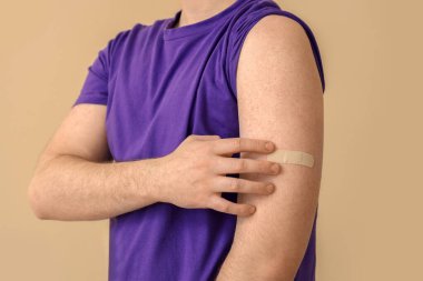 Bej arka planda uygulamalı tıbbi yaması olan erkek kol, yakın plan. Aşılama kavramı