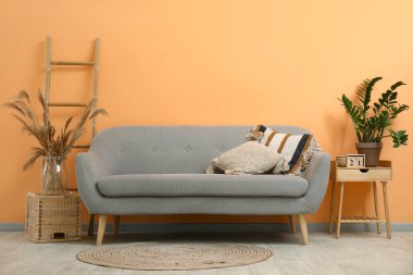 Yastıklı gri kanepe, ahşap merdiven, şeftali duvarının yanındaki taburede saksı ve otlar.