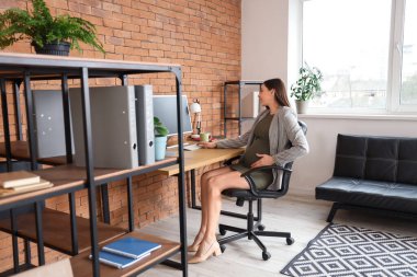 Ofiste bilgisayarla çalışan hamile bir iş kadını.