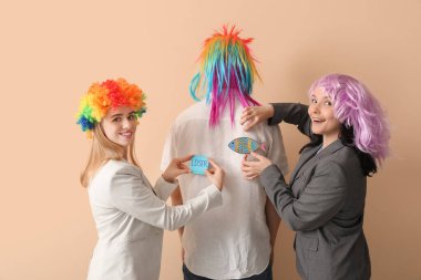 Genç kadınlar, bej arka planda iş arkadaşlarının sırtına kağıt yapıştırıyorlar. 1 Nisan Kutlaması