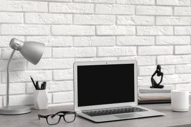 Beyaz duvarın yanında lamba ve dizüstü bilgisayarı olan modern işyeri