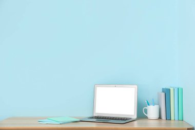 Mavi duvarın yanında kitapları ve dizüstü bilgisayarı olan şık bir iş yeri