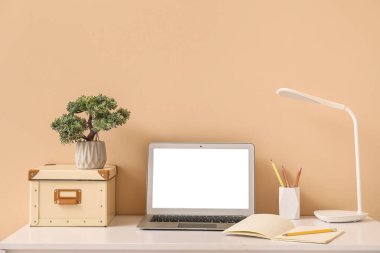 Bej duvarın yanında lamba, kitap ve dizüstü bilgisayarı olan güzel bir iş yeri