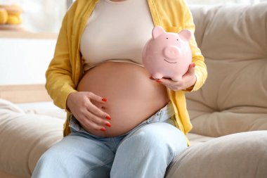 Kumbarası olan hamile bir kadın evde oturuyor, yakın plan. Annelik Faydası kavramı