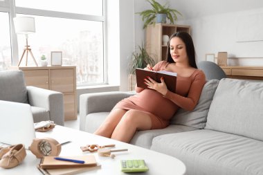 Evdeki not defterine yazan hamile bir kadın. Annelik Faydası kavramı