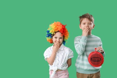 Renkli palyaço peruğu ve yeşil arka planda gülen osuruk yastığı olan küçük kardeş ve kardeş. 1 Nisan şakası