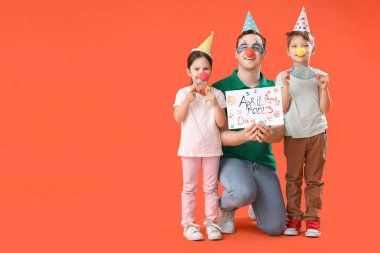 Babam ve komik kılık değiştiren küçük çocukları ve turuncu arka planda kağıt balıklar. 1 Nisan şakası