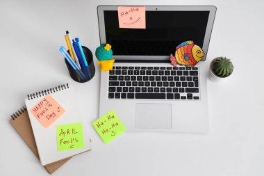 Bilgisayarlı çalışma alanı, komik yapışkan notlar ve beyaz arka planda kağıt balık. 1 Nisan şakası.