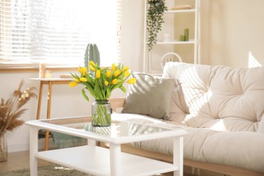 Oturma odasında lale vazosu olan rahat beyaz bir kanepe.