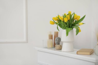 Sarı lalelerden oluşan güzel bir vazo. Mumlar ve kitap oturma odasında.