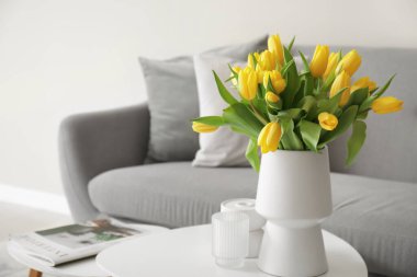Gri kanepesi ve kahve masasında sarı laleleri olan modern oturma odası.