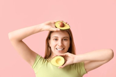 Pembe arka planda avokadosu olan güzel bir genç kadın.