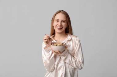 Gri arka planda bir kase sağlıklı yulaf ezmesi olan genç bir kadın.