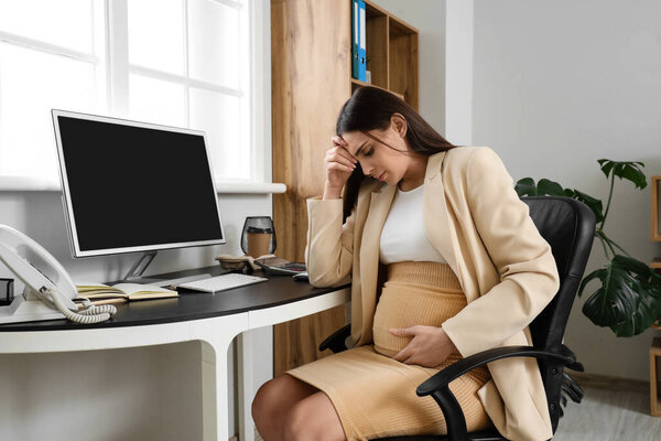 Tired young pregnant businesswoman sitting in office