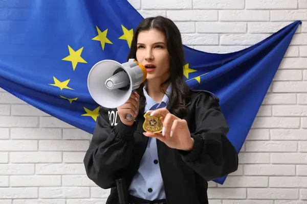 Female police officer with megaphone and flag of EU on white brick background