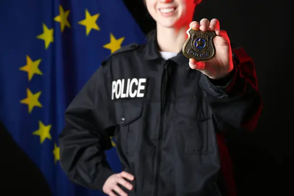 Female police officer with shield and flag of EU on dark background
