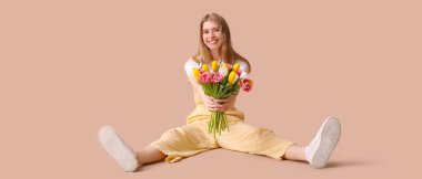 Bej arka planda oturan güzel lalelerle dolu buketi olan güzel genç bir kadın. 